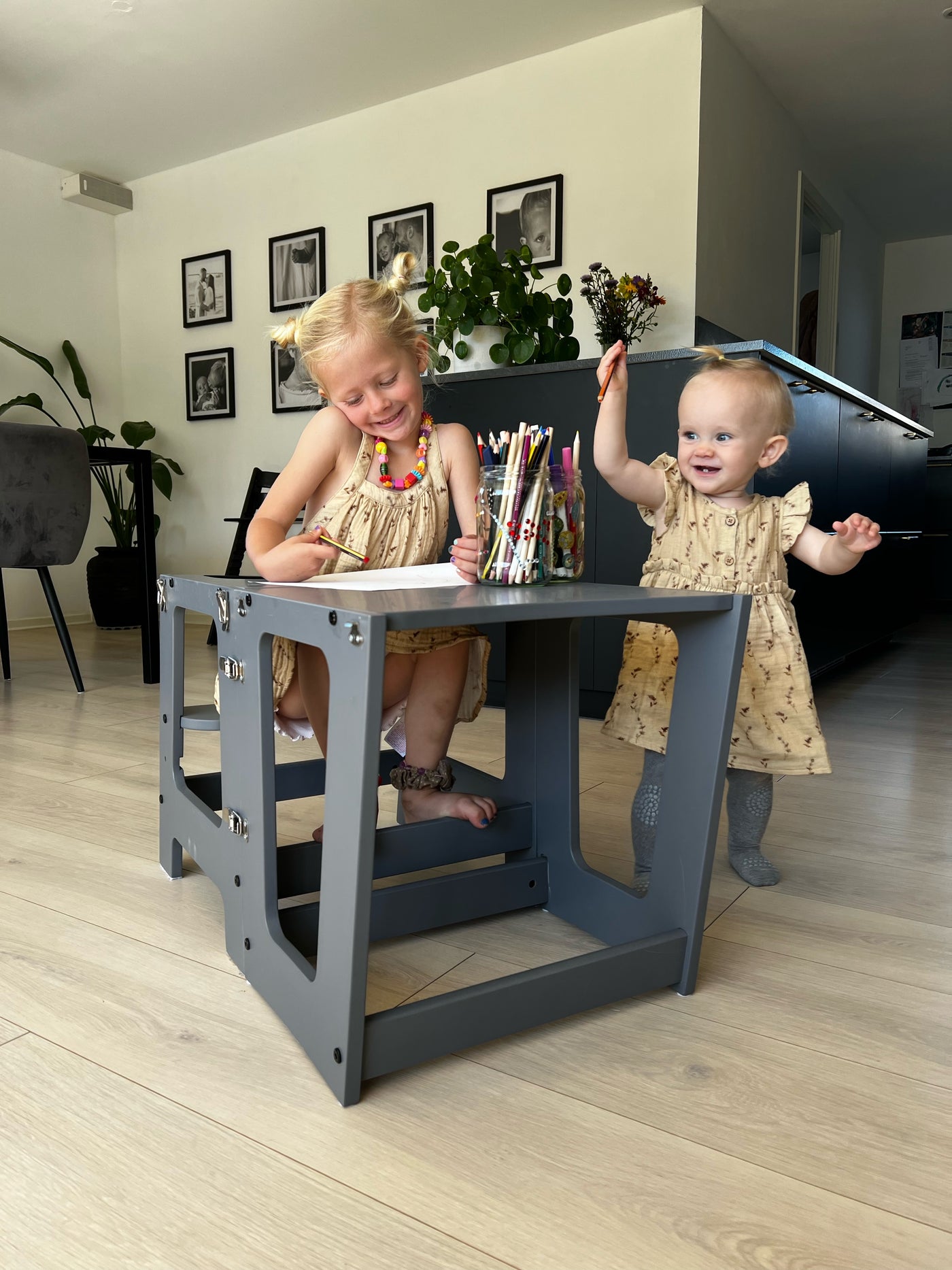 lille pige står og griner ved siden af et udfoldet læringstårn, hvor en anden pige sidder og tegner