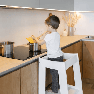 Dreng hjælper til med madlavningen i sit hvide læringstårn