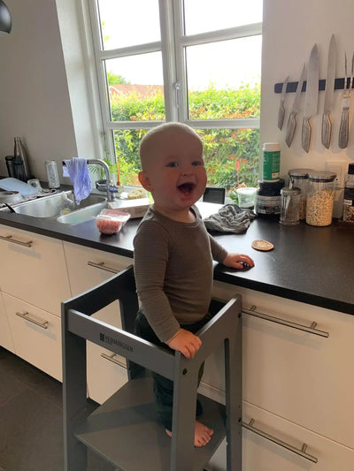 Dreng i grå trøje smiler fra sit læringstårn i køkken