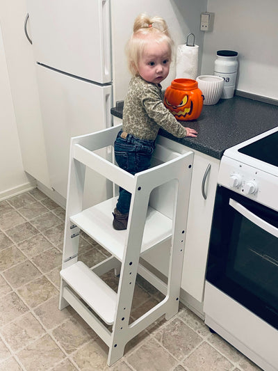 Lille pige står i sit hvide læringstårn med krukke i køkkenet