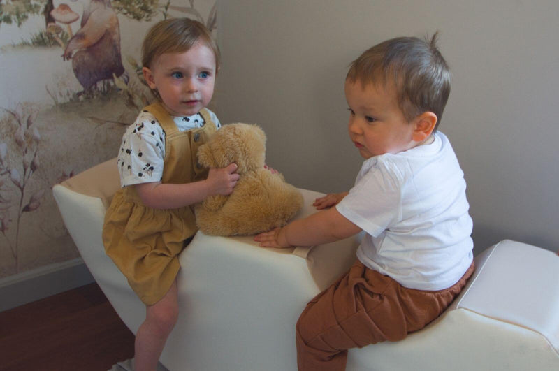 to små børn sidder på skum vippen sammen med en lille bamse